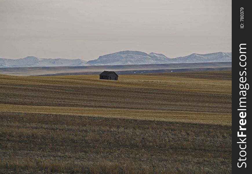 This picture was taken near Choteau, MT during a back country road drive and depicts an abandoned building in a large cultivated area with mountains in the background. This picture was taken near Choteau, MT during a back country road drive and depicts an abandoned building in a large cultivated area with mountains in the background.