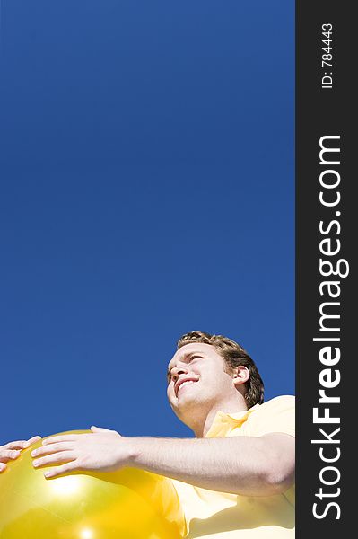 Happy Man holds a big, yellow ball and looks off to the distance under a blue sky