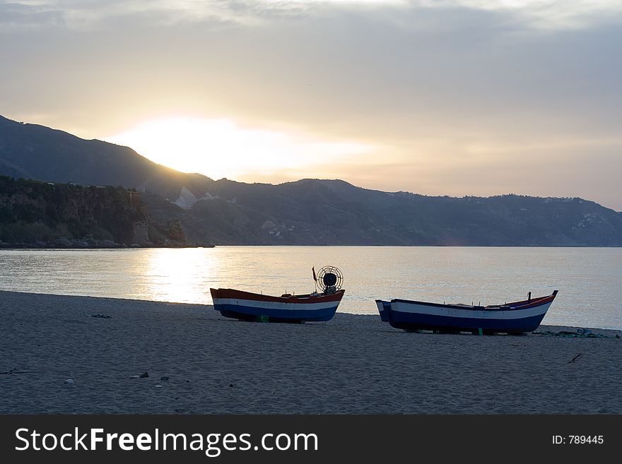 The day breaks over two boats pulled up on a mediterannean beach. The day breaks over two boats pulled up on a mediterannean beach