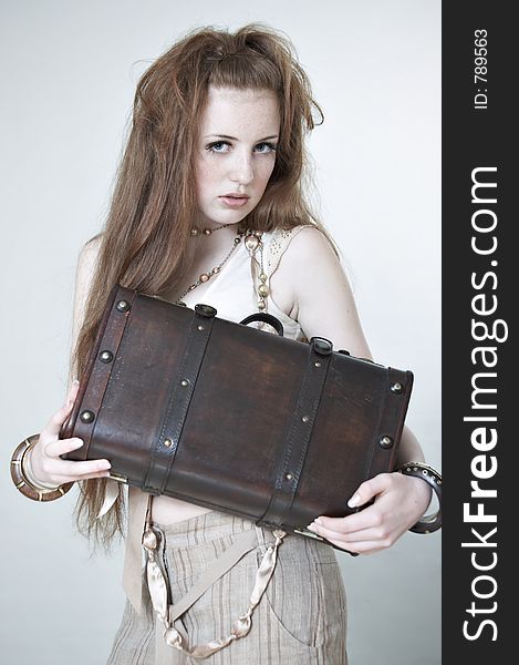 A girl with red hair. She holds a wooden suitcase in hands. The photo is executed in beige and warm tones. Studio. A girl with red hair. She holds a wooden suitcase in hands. The photo is executed in beige and warm tones. Studio