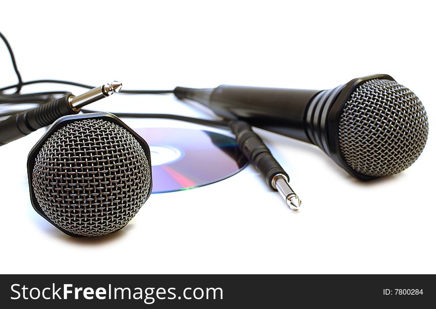 Two black wired karaoke microphones with gray metal grill on isolated background and CD (DVD) disk. Two black wired karaoke microphones with gray metal grill on isolated background and CD (DVD) disk.