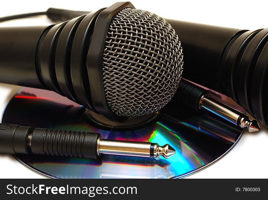 Two black wired karaoke microphones with gray metal grill on isolated background and CD (DVD) disk. Two black wired karaoke microphones with gray metal grill on isolated background and CD (DVD) disk.