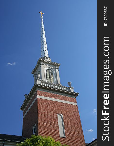 A traditional-style church steeple topped by a cross rises into a brilliant blue sky, with a few nice-day white clouds.

Focus is on the steeple & cross.
Includes copy space.
Please use respectfully.