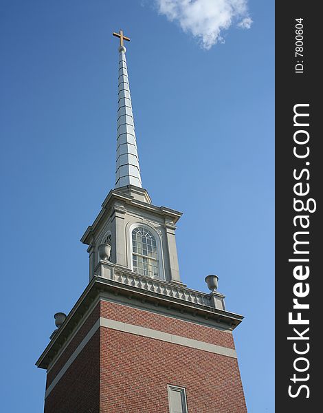 A traditional-style church steeple topped by a cross rises into a brilliant blue sky, with a few nice-day white clouds. Focus is on the steeple & cross. Includes copy space. Please use respectfully.