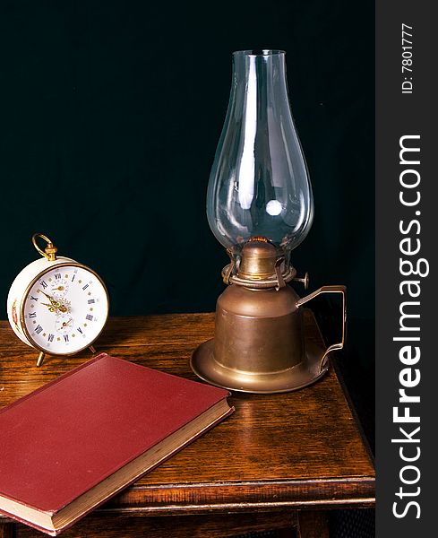 A book, kerosene lamp and alarm clock on a bedside table. A book, kerosene lamp and alarm clock on a bedside table