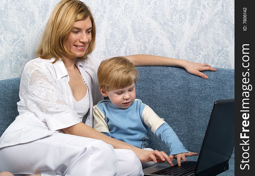 Young mum with the small beautiful boy together sit near laptop. Young mum with the small beautiful boy together sit near laptop