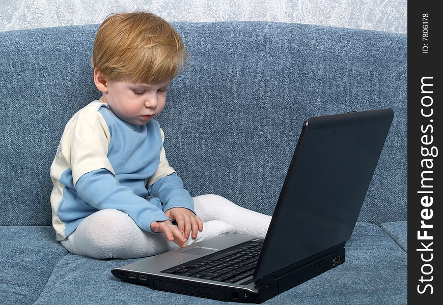 The little boy sits near the closed laptop. The little boy sits near the closed laptop