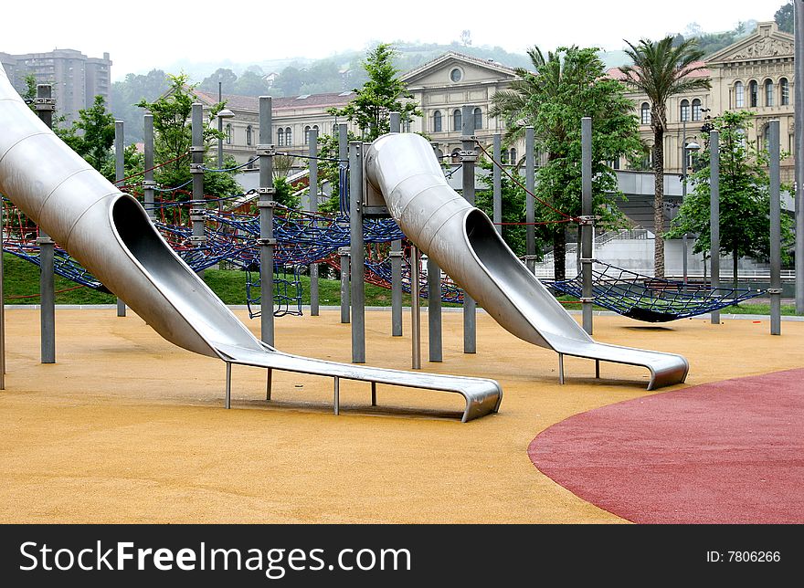 A child friendly play area with chutes and rope ladders in the centre of Bilbao in spanish Basque Country. Green trees and palms are surrounding the children's playground. A child friendly play area with chutes and rope ladders in the centre of Bilbao in spanish Basque Country. Green trees and palms are surrounding the children's playground.