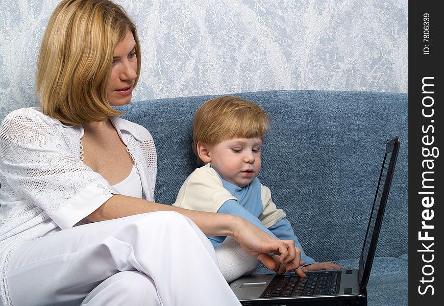 Young mum with the small beautiful boy together sit near laptop. Young mum with the small beautiful boy together sit near laptop