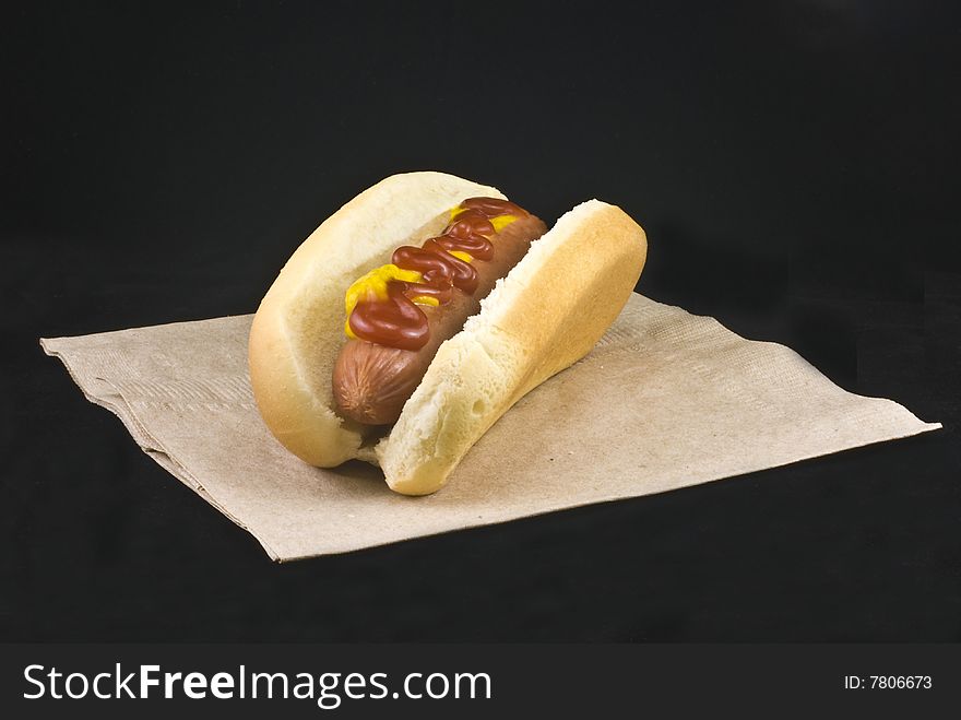 Hotdog with ketchup and mustard in a hotdog bun on a black background.