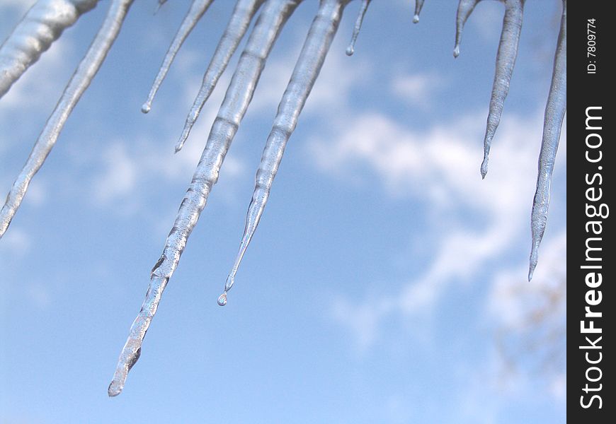 Melting icicles against blue sky on edge of roof