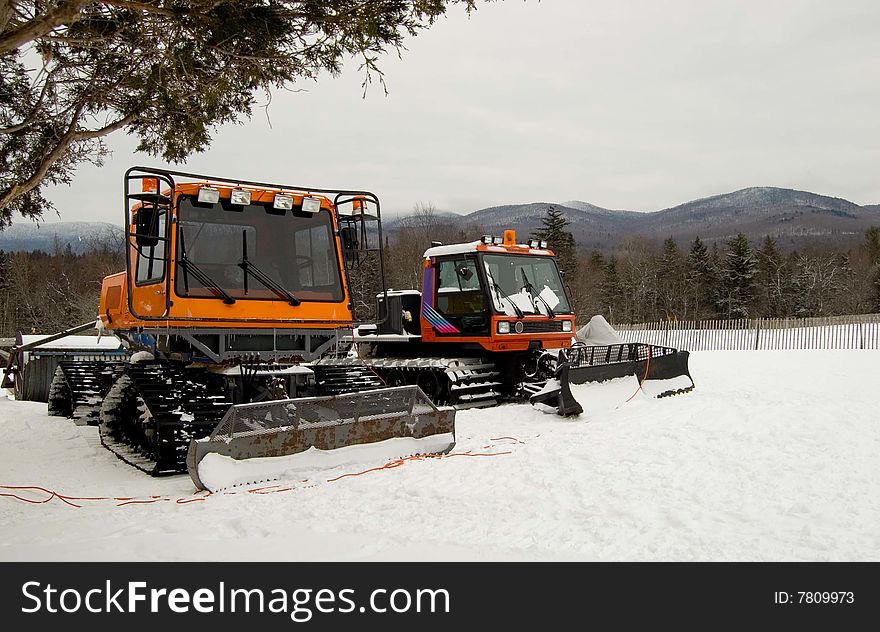 Two ski trail groomers with mountains in background