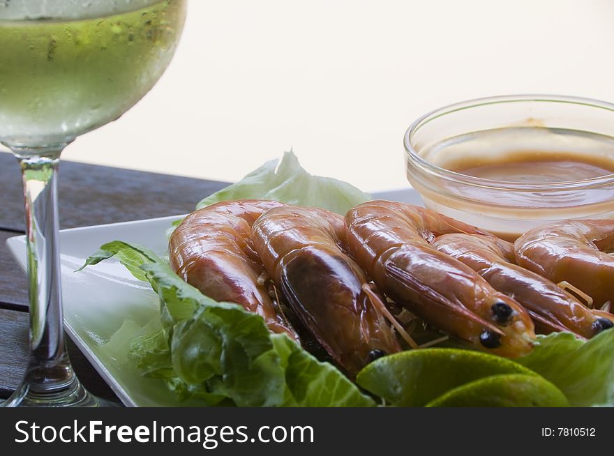 Fresh king prawns placed on a bed of lettuce served with a pink sauce and slices of lemons accompanied by a glass of white wine in an outdoor setting.