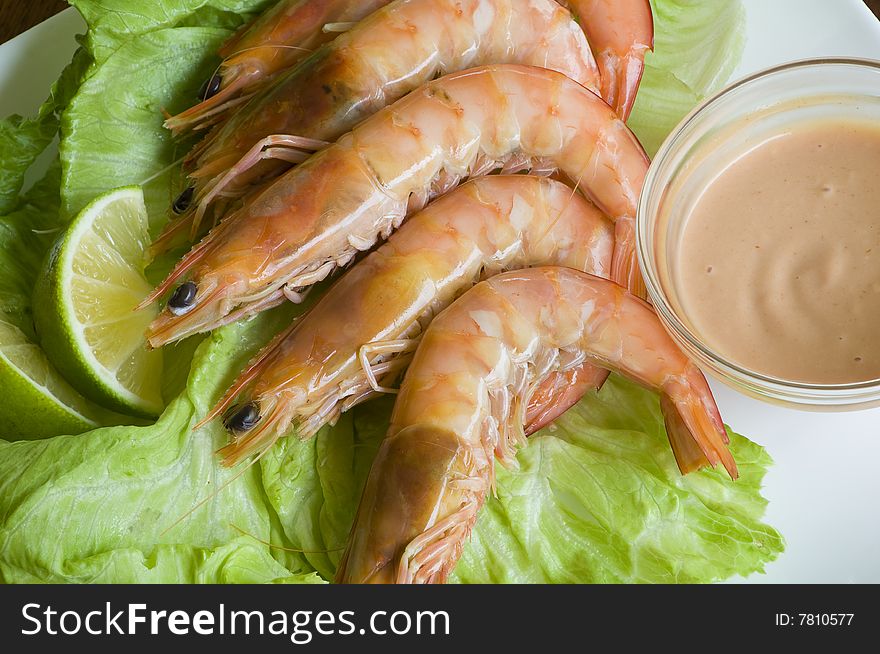 Fresh king prawns placed on a bed of lettuce served with a pink sauce and slices of lemons accompanied by a glass of white wine in an outdoor setting.