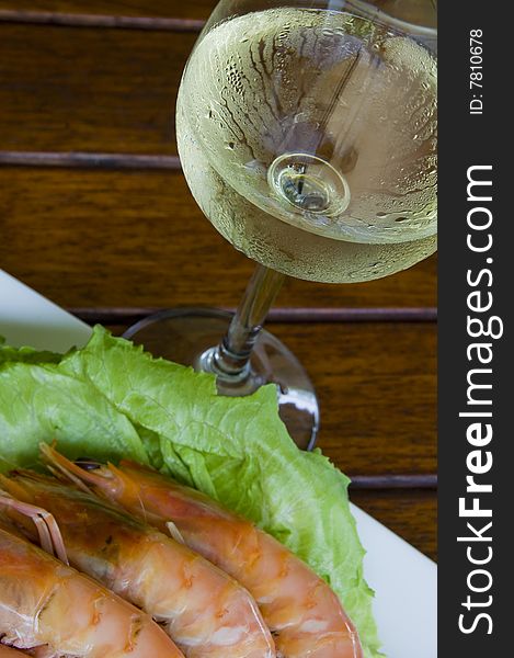 Fresh king prawns placed on a bed of lettuce served with a pink sauce and slices of lemons accompanied by a glass of white wine in an outdoor setting.