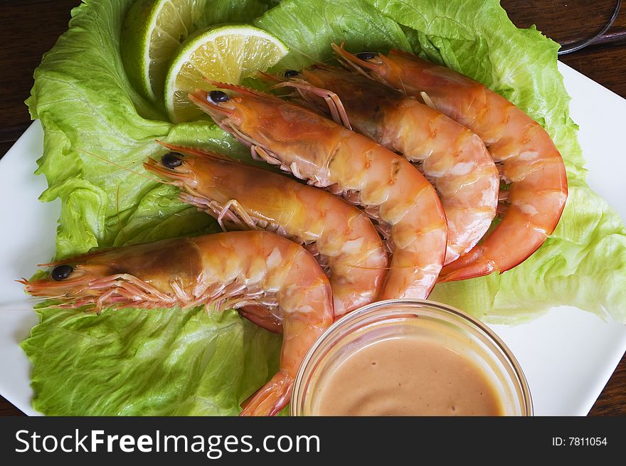 Fresh king prawns placed on a bed of lettuce served with a pink sauce and slices of lemons accompanied by a glass of white wine in an outdoor setting.