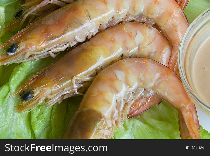 Fresh king prawns placed on a bed of lettuce served with a pink sauce and slices of lemons accompanied by a glass of white wine in an outdoor setting.