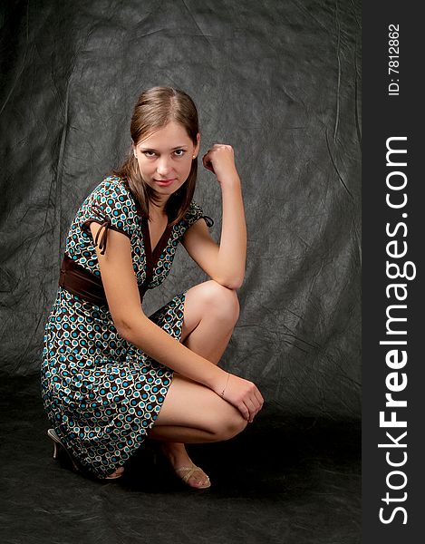 Young girl in color dress with white skin straight dark hair sitting turned left side with head turned with naked legs and free pose isolated on black. Young girl in color dress with white skin straight dark hair sitting turned left side with head turned with naked legs and free pose isolated on black