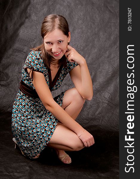Young white girl in color dress sitting on her hunkers turned slightly smiling isolated on black