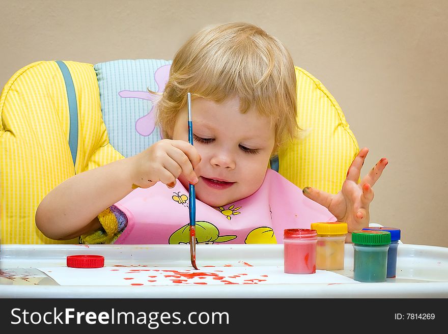 The child of 2 years sits in a children's chair and draws paints. The child of 2 years sits in a children's chair and draws paints