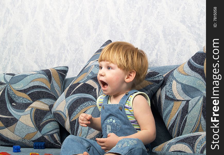 The little boy sits on a sofa expressing emotion. The little boy sits on a sofa expressing emotion