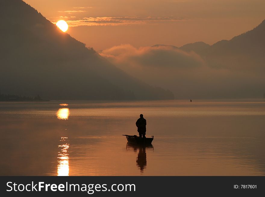 Lonely fisherman on the lake, sunset in the background. Lonely fisherman on the lake, sunset in the background