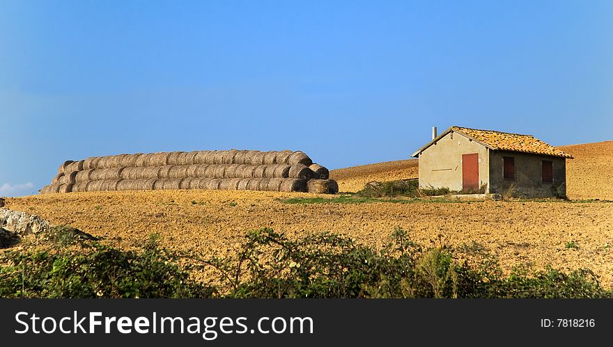 House in field with hay rolls. Copy space in blue sky. House in field with hay rolls. Copy space in blue sky