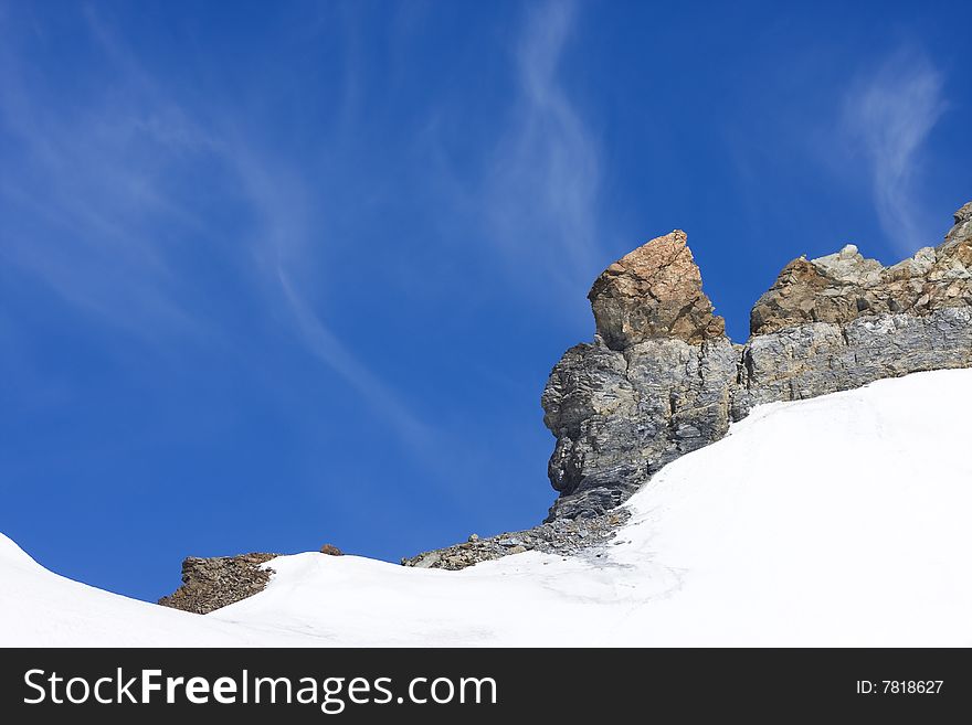 Snow landscape with rocks in Swiss Alps, bright blue sky in background with copy-space