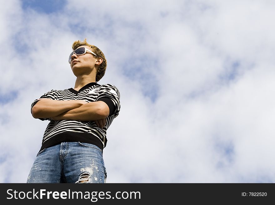 Young beautiful man model standing under the cloudy sky. Blue cloudy sky background.