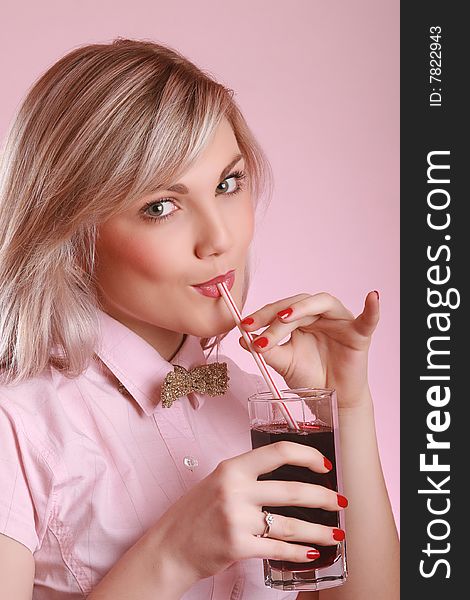 Attractive young woman drinking juice isolated on pink background