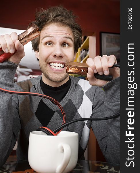 Young man holding jumper cables coming out of coffee mug. Young man holding jumper cables coming out of coffee mug