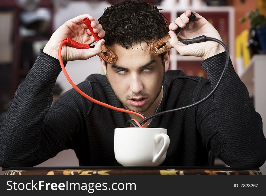 Young man holding jumper cables coming out of coffee mug. Young man holding jumper cables coming out of coffee mug