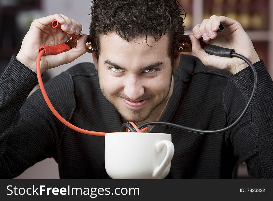 Young man holding jumper cables coming out of coffee mug. Young man holding jumper cables coming out of coffee mug
