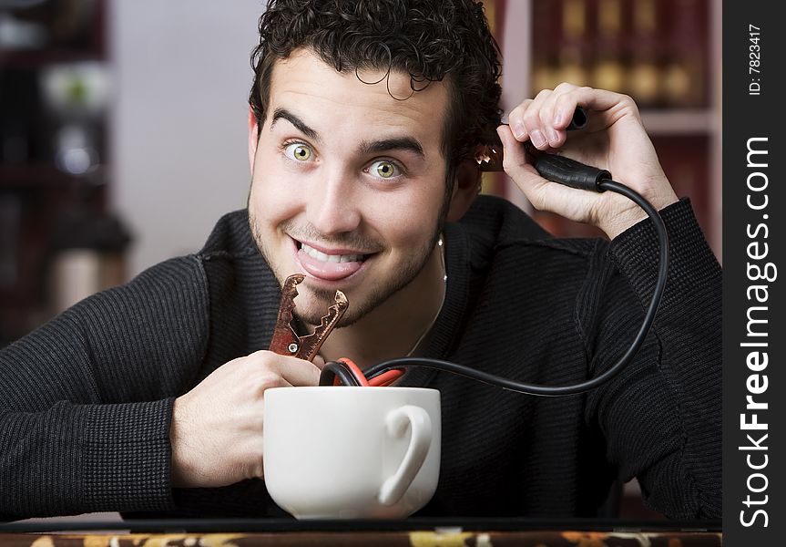 Young man holding jumper cables coming out of coffee mug. Young man holding jumper cables coming out of coffee mug