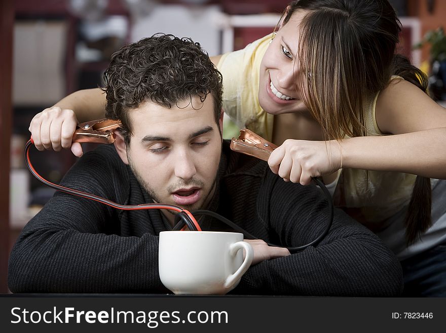 Young woman holding jumper cables coming out of coffee mug to man's head. Young woman holding jumper cables coming out of coffee mug to man's head