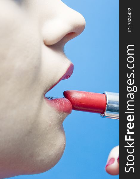 Closeup of a woman applying lipstick on a blue background