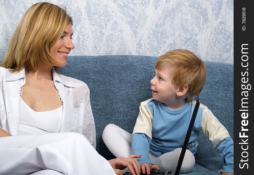 Young mum with the small beautiful boy together sit near laptop. Young mum with the small beautiful boy together sit near laptop