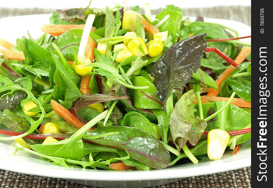 A bowl baby greens, strips of carrots and sweet corn dressed with olive oil and vinegar. A bowl baby greens, strips of carrots and sweet corn dressed with olive oil and vinegar.