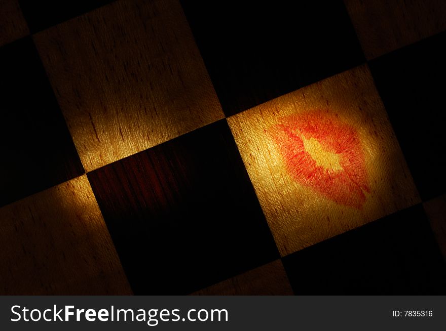 Lipstick mark on a selectively illuminated checkered wooden surface. Image is a real photograph. Lipstick mark on a selectively illuminated checkered wooden surface. Image is a real photograph.