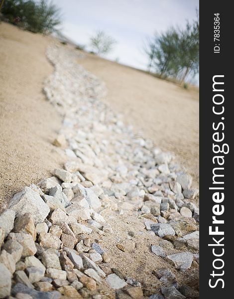 A rock path made of many different tan rocks and sand line a simple path down a hill