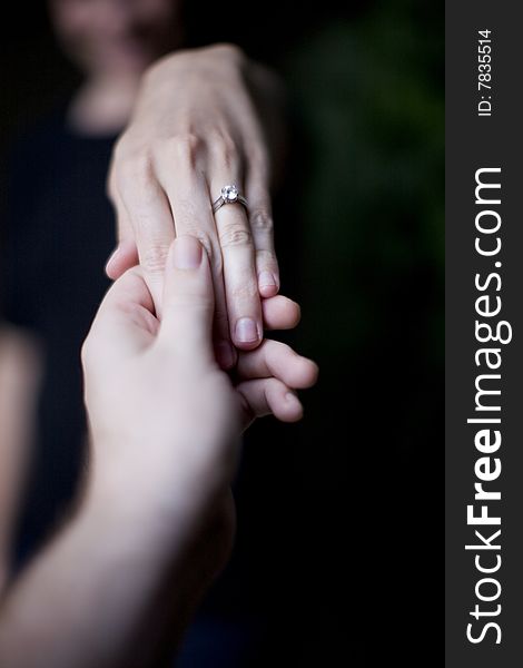 A woman holds her hand up to show her wedding ring as a man holds her hand up to see the ring. A woman holds her hand up to show her wedding ring as a man holds her hand up to see the ring