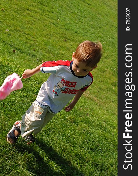 Child with cotton candy running on green grass field