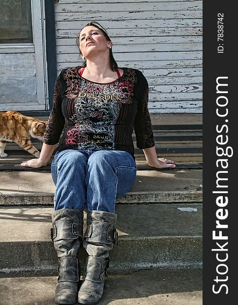 A female wearing jeans and boots sitting on a porch waiting for something. A female wearing jeans and boots sitting on a porch waiting for something.