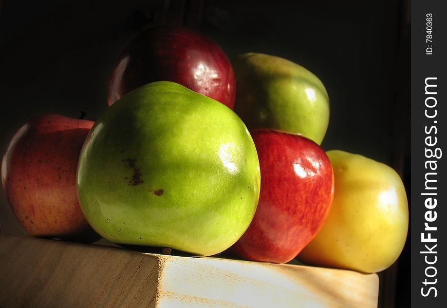 Some colorful apples on wooden board under cross-like shadows