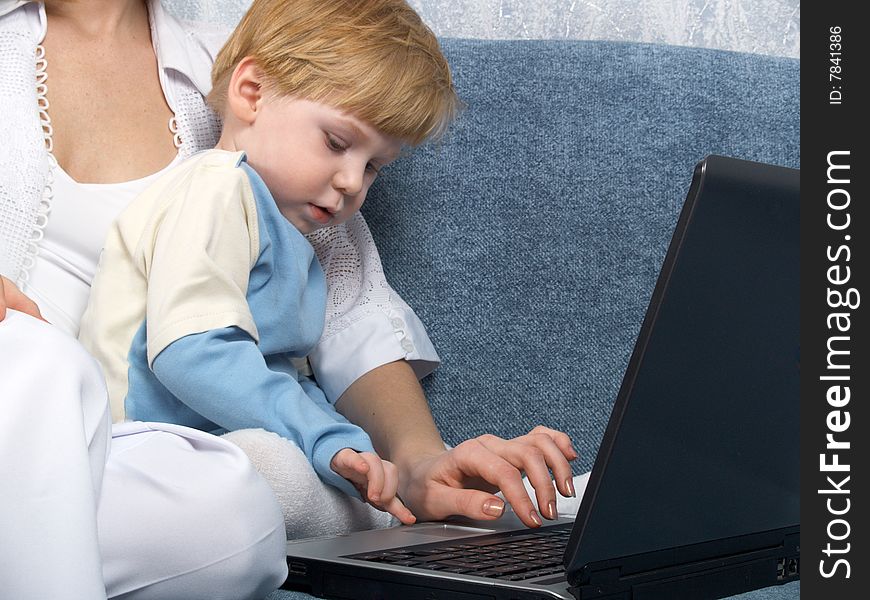 Young mum with the small beautiful boy together sit near laptop. Young mum with the small beautiful boy together sit near laptop