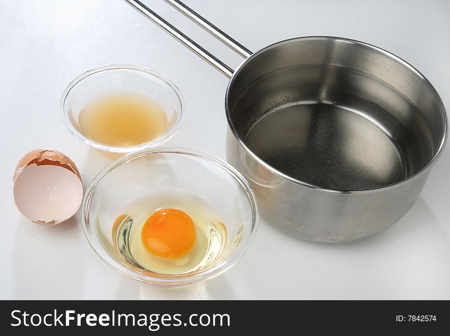 Cracked egg in bowl and water in pan on table