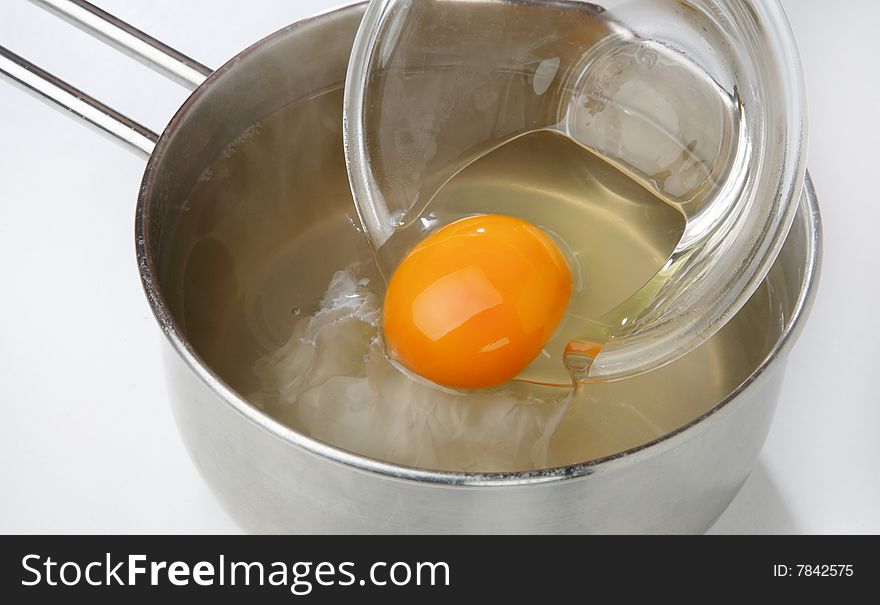 Cracked egg in bowl and water in pan on table