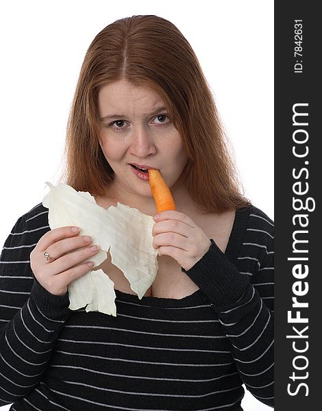 The young woman eats carrots and holds cabbage sheet. The young woman eats carrots and holds cabbage sheet