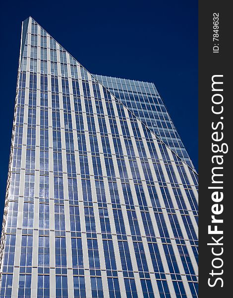 A modern blue glass office tower rising against a blue sky. A modern blue glass office tower rising against a blue sky