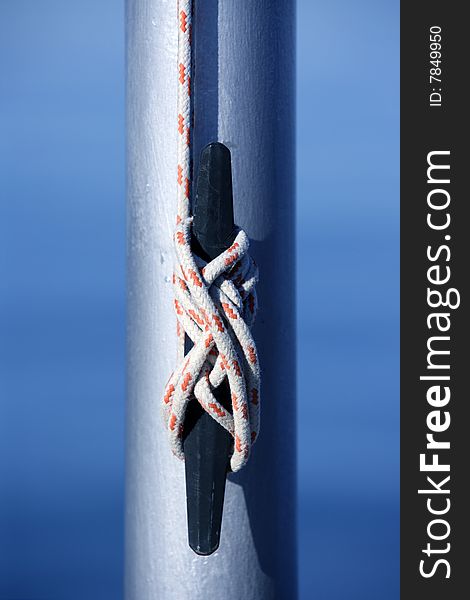 Marine rope, knot arround a steel pole, blue water background